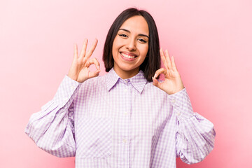 Young hispanic woman isolated on pink background cheerful and confident showing ok gesture.