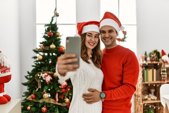 Young hispanic couple smiling happy wearing christmas hat making selfie by the smartphone at home.