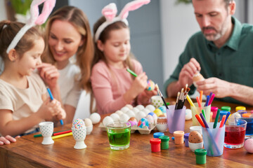 Happy caucasian family of four people decorates easter eggs at home