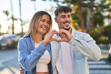 Naklejka premium Young man and woman couple smiling confident doing heart symbol with hands at street