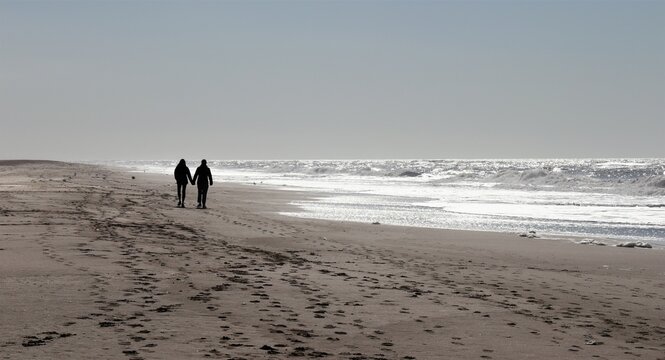 Silhouette of a couple walking hand in hand on a deserted beach in the morning
