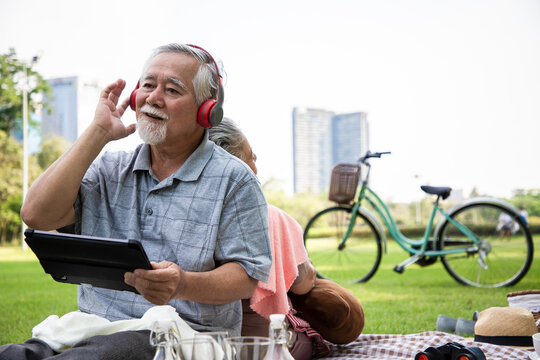 An elderly couple doing picnics and relaxing in the garden with bright smiles and enjoying the relaxation of classical music. Health and relaxation after retirement. - Powered by Adobe