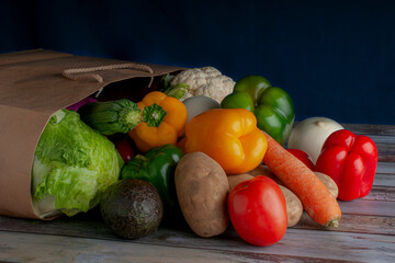 A recycled paper bag from the grocery store full of vegetables, concept of healthy food on a wooden vintage table. Blue background horizontal