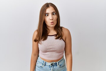 Young brunette woman standing over isolated background making fish face with lips, crazy and comical gesture. funny expression.