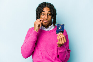 Young African American informatic man isolated on blue background with fingers on lips keeping a...