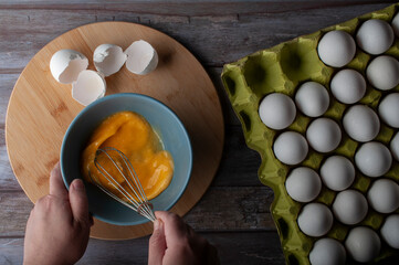 Scrambling eggs in a blue bowl with a group of eggs and eggs shell on the side. overhead top view...