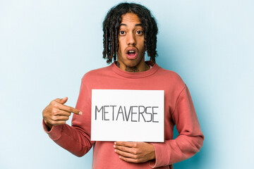 Young African American man holding metaverse placard isolated on blue background pointing to the side