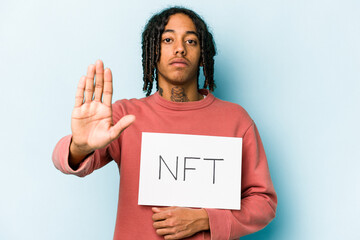 Young African american man holding NFT placard isolated on blue background standing with outstretched hand showing stop sign, preventing you.