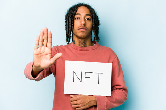 Young African american man holding NFT placard isolated on blue background standing with outstretched hand showing stop sign, preventing you.
