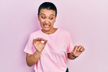 Beautiful hispanic woman with short hair wearing casual pink t shirt disgusted expression,...