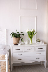 White tulips and a green indoor flower stand on the bedside table next to tea dishes