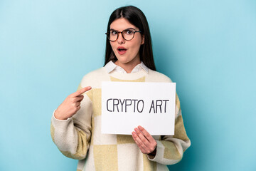 Young caucasian business woman holding a crypto art placard isolated on blue background pointing to the side