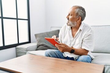 Senior grey-haired man smiling confident using touchpad at home