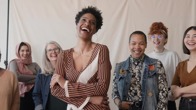 Slow motion of cheerful mature black woman with multiethnic friends smiling and looking at camera in celebration of International Women's Day