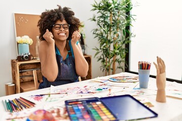 Beautiful african american woman with afro hair painting at art studio excited for success with arms raised and eyes closed celebrating victory smiling. winner concept.