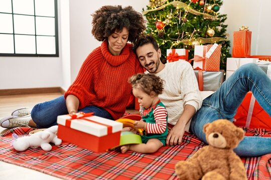 Couple and daughter holding gift sitting by christmas tree at home