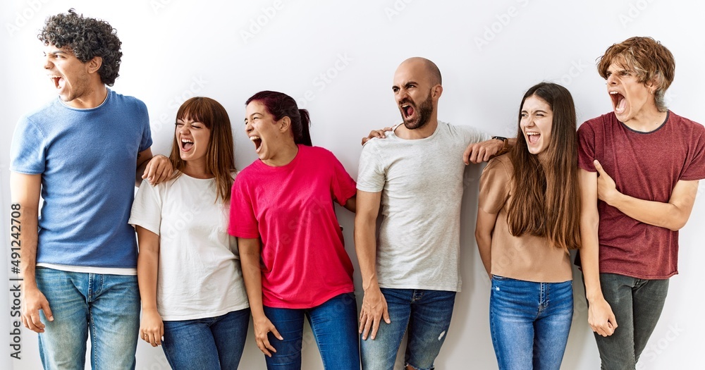 Poster group of young friends standing together over isolated background angry and mad screaming frustrated