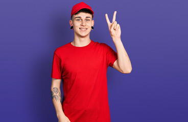 Young caucasian boy with ears dilation wearing delivery uniform and cap smiling with happy face...