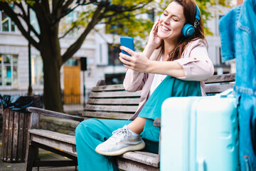 Smiling woman listening music and using smart phone on bench