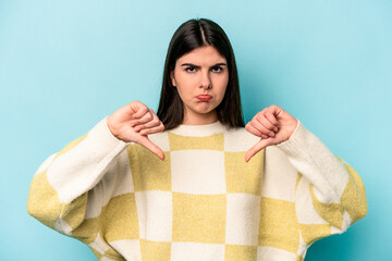 Young caucasian woman isolated on blue background showing a dislike gesture, thumbs down....