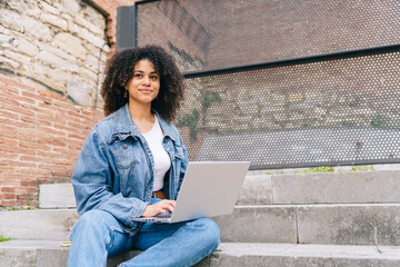 Thoughtful young woman with laptop sitting on steps