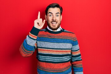 Fototapeta premium Handsome caucasian man with beard wearing elegant wool winter sweater pointing finger up with successful idea. exited and happy. number one.