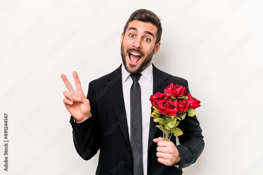 Wall mural Young caucasian man holding a bouquet of flowers isolated on white background joyful and carefree showing a peace symbol with fingers.