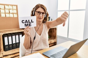 Middle age brunette woman wearing operator headset holding call me banner looking unhappy and angry showing rejection and negative with thumbs down gesture. bad expression. © Krakenimages.com