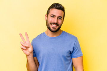 Young caucasian man isolated on yellow background showing victory sign and smiling broadly.