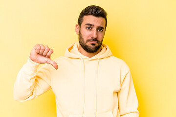 Young caucasian man isolated on yellow background showing a dislike gesture, thumbs down....
