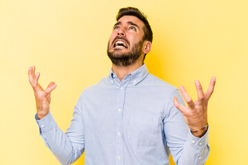 Young caucasian man isolated on yellow background screaming to the sky, looking up, frustrated.