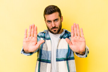 Young caucasian man isolated on yellow background standing with outstretched hand showing stop...