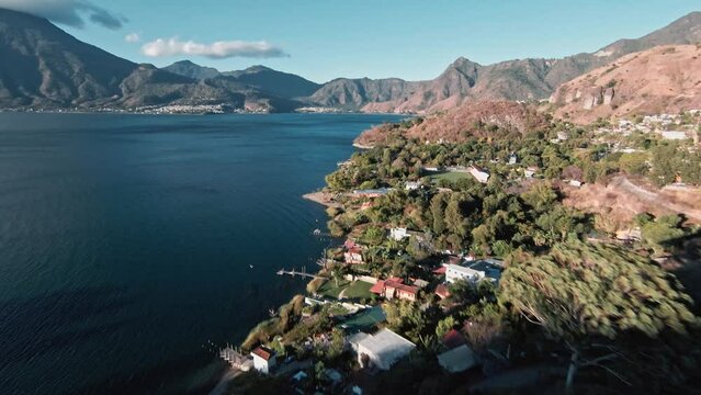 Small coastal town to lake Atilan and massive volcano mount with cloud cap on side, aerial FPV view