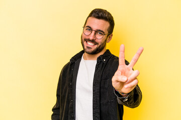 Young caucasian man isolated on yellow background joyful and carefree showing a peace symbol with fingers.