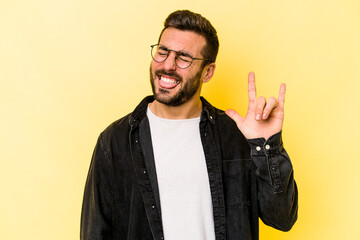 Young caucasian man isolated on yellow background showing rock gesture with fingers