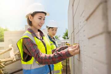 Beautiful Asian woman engineer inspection AAC Brock to quality control.Work tools put on a autoclaved aerated concrete blocks wall.Inspector use a tape measure to check the size of the block.Team work