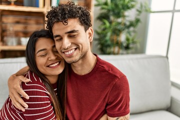 Obraz premium Young latin couple smiling happy and hugging sitting on the sofa at home.