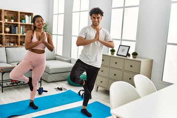 Fototapeta premium Young latin couple smiling happy training yoga pose at home.
