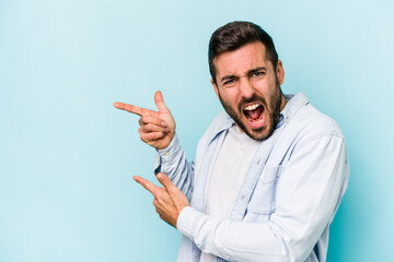 Young caucasian man isolated on blue background pointing with forefingers to a copy space, expressing excitement and desire.