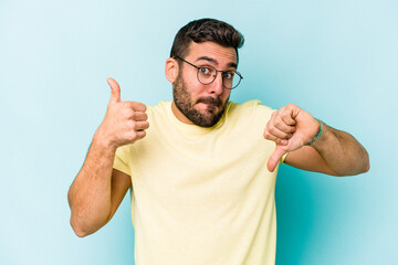 Fototapeta premium Young caucasian man isolated on blue background showing thumbs up and thumbs down, difficult choose concept