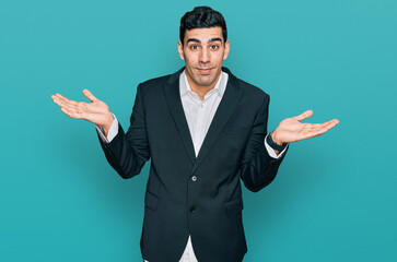 Handsome hispanic man wearing business clothes clueless and confused expression with arms and hands...
