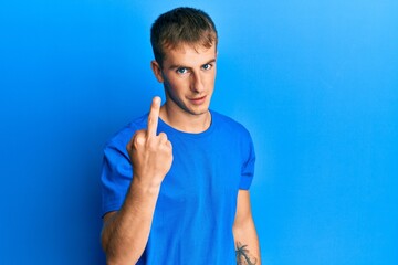 Young caucasian man wearing casual blue t shirt showing middle finger, impolite and rude fuck off expression