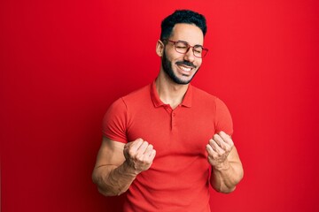 Fototapeta premium Young hispanic man wearing casual clothes and glasses excited for success with arms raised and eyes closed celebrating victory smiling. winner concept.