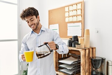 Young hispanic businessman smiling happy puoring jar of coffee at the office.