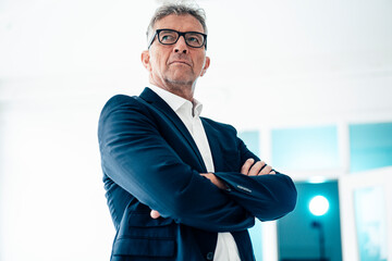 Confident businessman with arms crossed standing by white wall