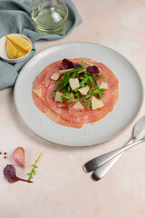 A dish with slices of thinly sliced meat, arugula and parmesan, seasoned with lemon juice and olive oil. Vertical frame
