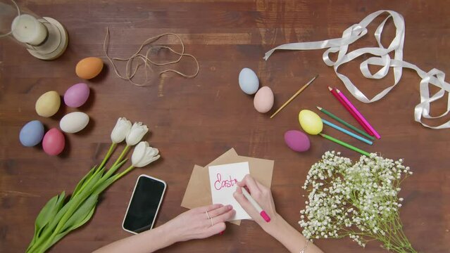 Top view of a table with items to create a composition for Easter. A woman's hand writes with a red marker: Easter menu. Christ is risen. Church holiday-Easter
