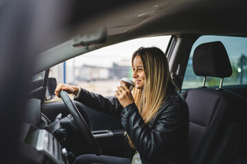 Young adult one caucasian woman driving car waiting while holding a cup of coffee looking on the road side view female driver copy space