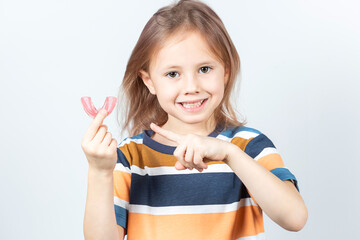 Cute little girl with blond hair is holding a pink dental myofunctional trainer