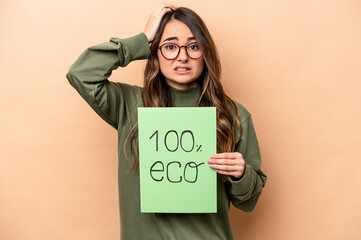 Young caucasian woman holding 100% eco placard isolated on beige background being shocked, she has...